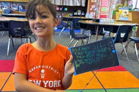 What's in this newsletter header image: Student holding a whiteboard from her reading lesson